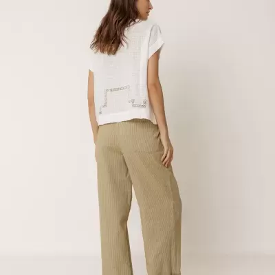 Mulher com blusa branca, calças largas bege e sapatos brancos vista de costas