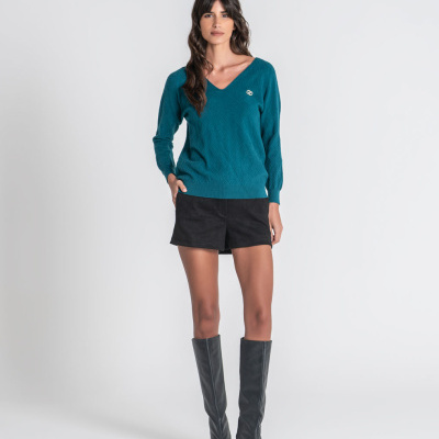Mulher com camisola azul petróleo, shorts pretos e botas pretas altas