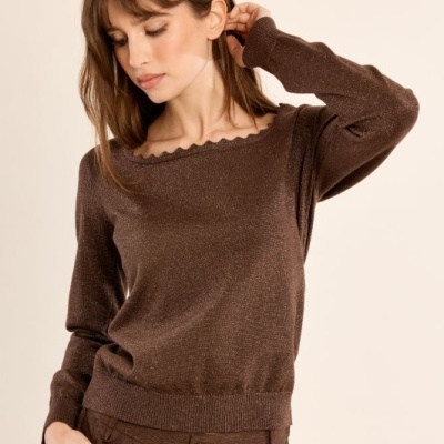 Mulher com camisola castanha e calças castanhas frente a fundo claro