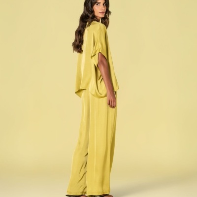 Conjunto amarelo claro com blusa de mangas curtas e calças largas, sandálias pretas de salto fino, fundo amarelo.