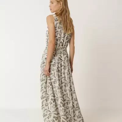 Vestido comprido floral em tons verdes e bege com cinto, sem mangas, usado com sandálias verdes em fundo branco.