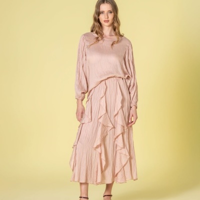 Modelo com conjunto rosa de blusa e saia com folhos e sandálias castanhas