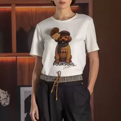 Mulher com t-shirt branca estampada, calças pretas e boné castanho com logo branco