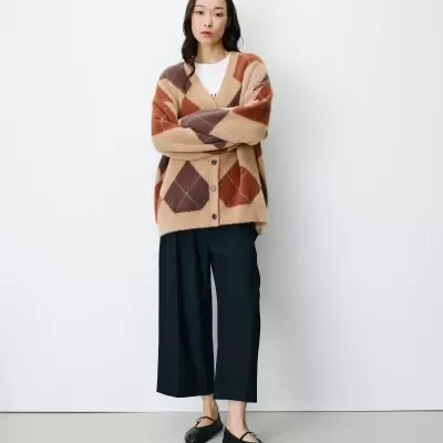 Mulher com casaco oversized xadrez castanho, calças pretas e sapatos negros, em fundo branco