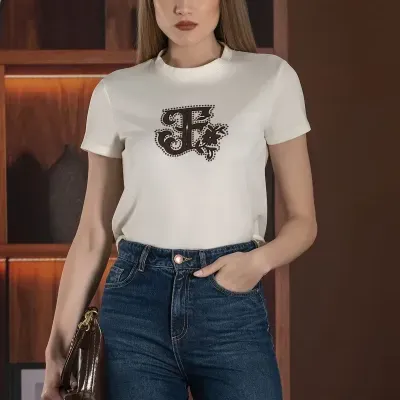 Mulher com t-shirt branca com estampado castanho e jeans escuros em ambiente interior com prateleiras de madeira