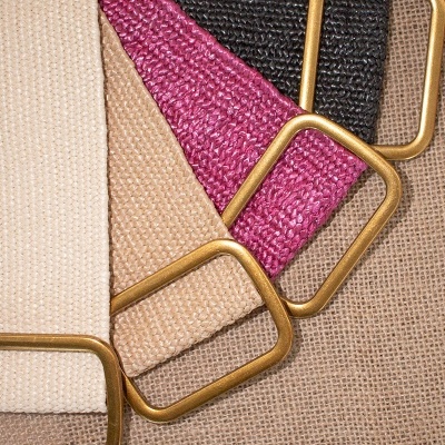 Quatro cintos têxteis com fivelas douradas e cores variadas sobre superfície texturizada.