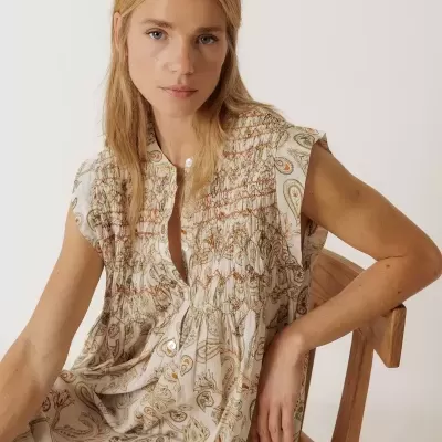 Vestido floral bege com padrões paisley e botões, sentado numa cadeira de madeira