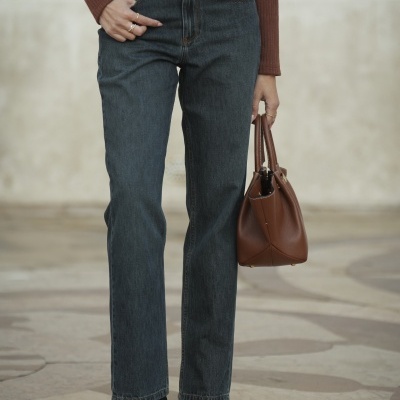 Calças jeans azuis com camisola castanha e mala castanha em ambiente exterior.
