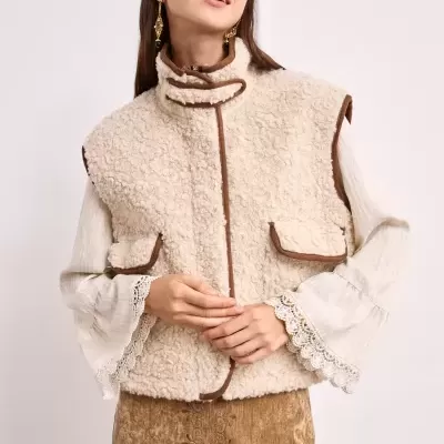 Mulher a usar colete de pêlo cru com detalhes castanhos, blusa branca de renda nas mangas e saia castanha bordada.