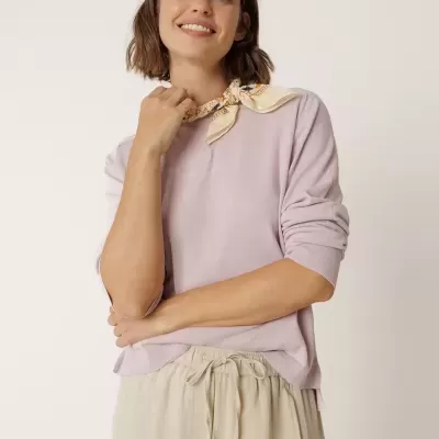 Pessoa com camisola lilás, calças bege e lenço creme com padrão floral.