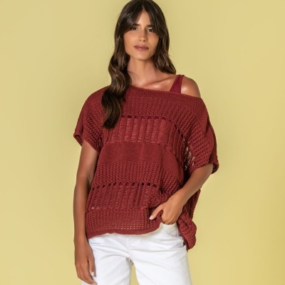 Mulher com camisola de malha castanha e calças brancas em fundo amarelo