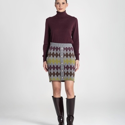 Mulher com camisola bordô de gola alta, saia padrão argyle com botões e botas pretas até ao joelho em estúdio