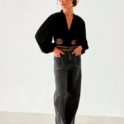 Mulher com blusa preta de mangas largas e calças de ganga cinza escuro