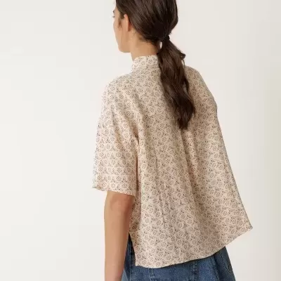 Camisa bege de manga curta com padrão floral e saia azul de ganga vista de costas