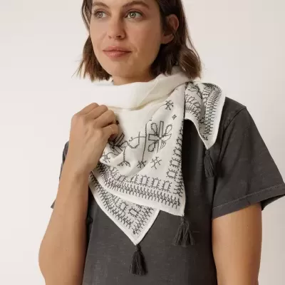 Cachecol branco com padrão bordado preto e tasséis pretos usado por mulher com vestido cinzento escuro