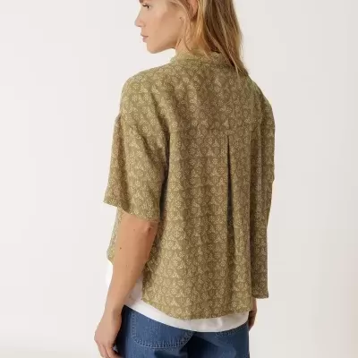 Mulher de costas a usar camisa verde com padrão geométrico e calções de ganga azul