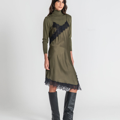 Vestido verde com renda preta usado com camisola verde de gola alta e botas pretas.