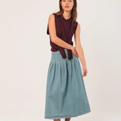 Mulher com camisola sem mangas vinho e saia midi azul clara num fundo branco