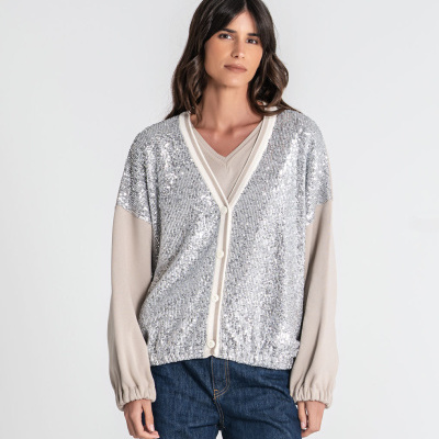 Mulher usando casaco de paetês prateados e mangas bege com botões, camisa bege e jeans azul