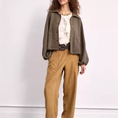 Mulher com casaco padrão, blusa creme com folhos, calças castanhas e sapatos castanhos