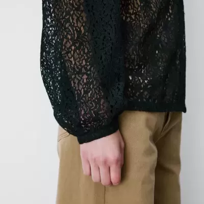 Manga preta de renda com padrão floral e calças bege.