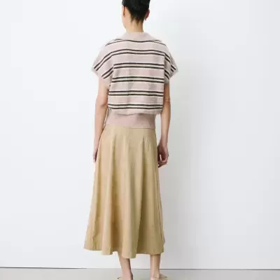 Mulher de costas com camisola riscada e saia bege em fundo branco