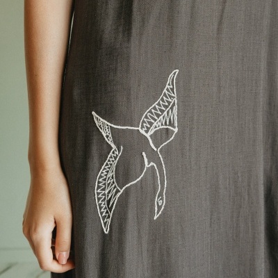 Vestido castanho escuro com bordado de pássaro branco e braço com pele clara visível.