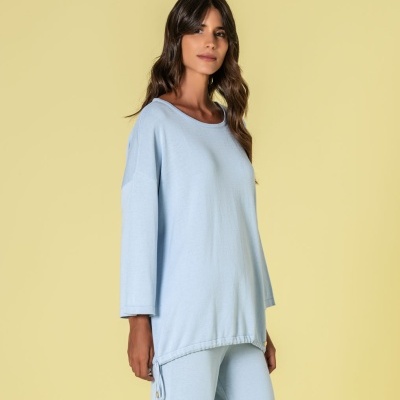 Conjunto azul claro de camisola e calças largas com cordões, usado por modelo em fundo amarelo