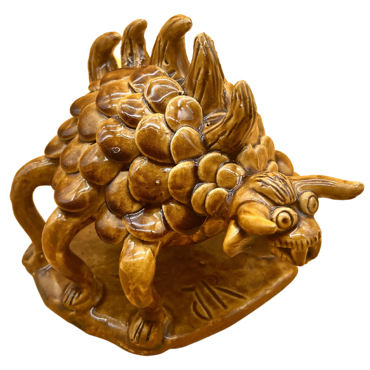Escultura cerâmica castanha de criatura fantástica com escamas e dentes, sobre base retangular.