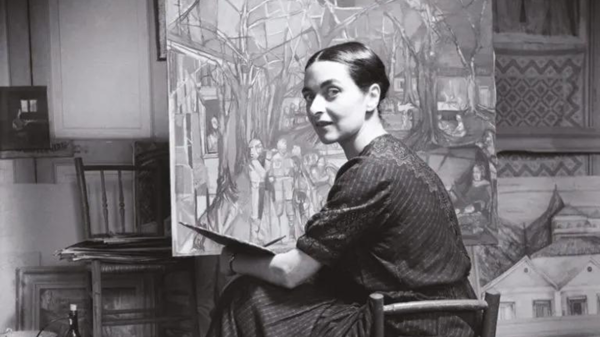 Mulher sentada a pintar junto a uma tela com pintura colorida