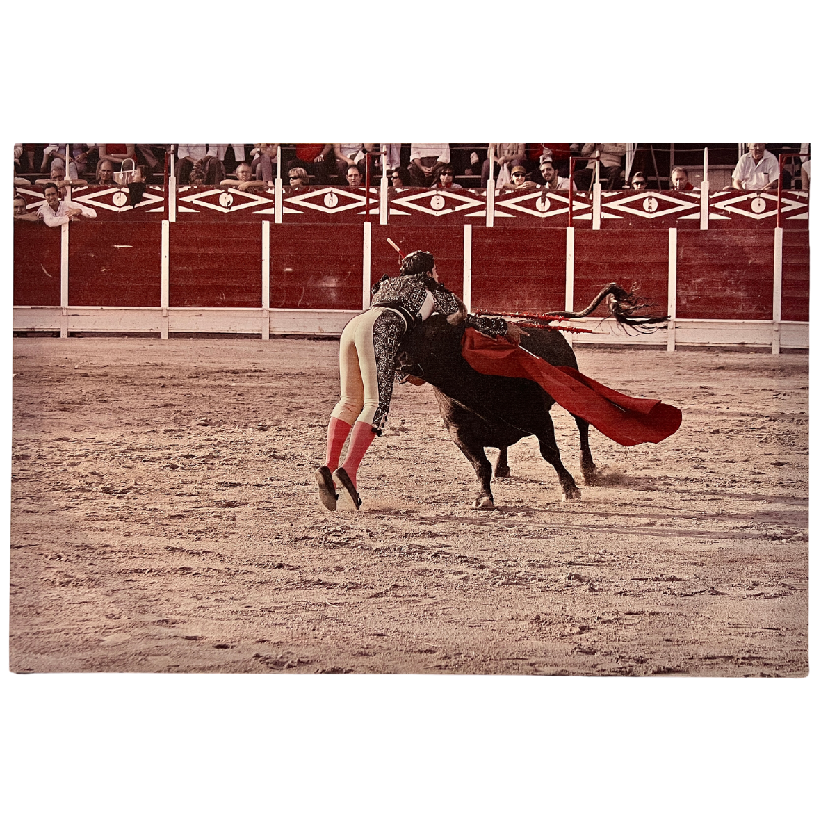 Toureiro vestido com casaca preta e calças claras encenando numa arena de touradas com público ao fundo