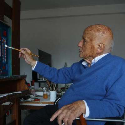 Idoso a pintar numa tela em cadeira de rodas num ambiente interior