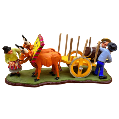 Figuras de madeira de pessoas, vacas alaranjadas e carro de madeira com barril sobre base verde