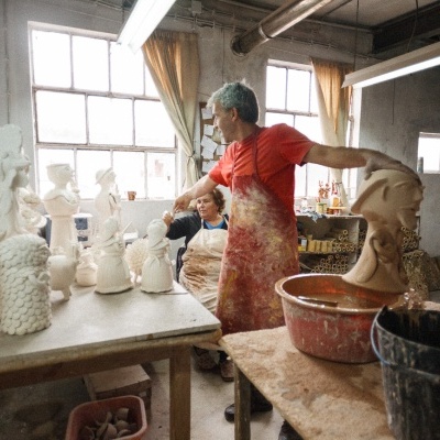 Oficina de escultura com duas pessoas e várias esculturas de gesso e barro