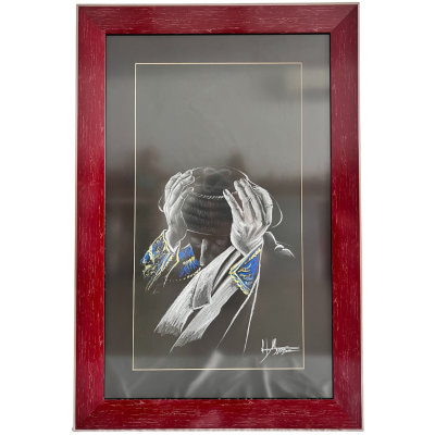 Quadro com moldura vermelha mostrando pessoa com capuz preto e casaco com detalhes azuis e dourados a cobrir o rosto com as mãos.