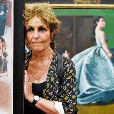 Mulher em galeria de arte com pinturas coloridas ao fundo.