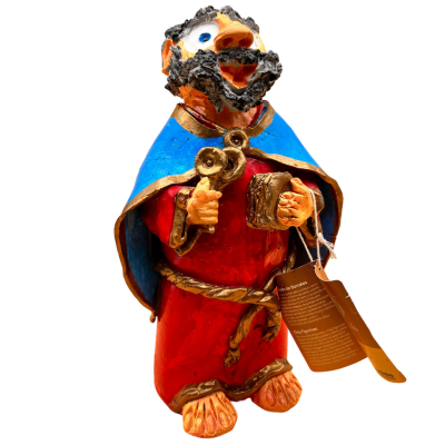 Figura decorativa de personagem com barba, túnica vermelha e capuz azul segurando um livro e uma chave, com etiqueta pendurada