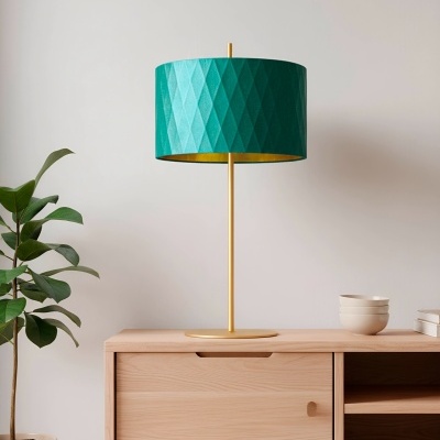 Candeeiro de mesa dourado com cúpula verde em móvel de madeira clara, planta ao lado