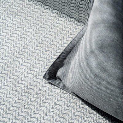 Almofada cinzenta em tapete com padrão ziguezague cinzento e branco