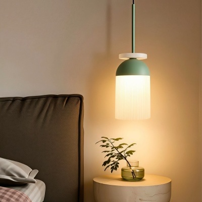 Abajur pendente verde com vidro branco sobre mesa de cabeceira creme e cama com cabeceira castanha.