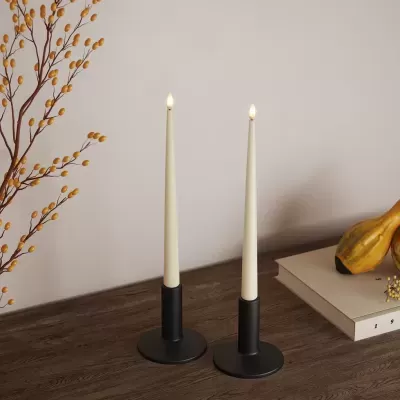 Castiçais pretos com velas brancas acesas sobre mesa de madeira com decoração ao redor.