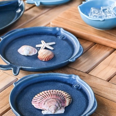Pratos e recipiente azuis de cerâmica com conchas decorativas na mesa de madeira