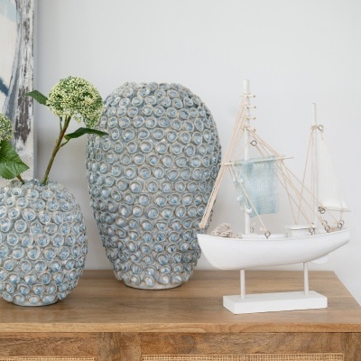 Dois vasos de cerâmica azuis com relevo circular e barco decorativo branco sobre móvel de madeira