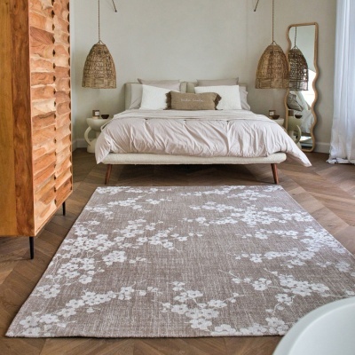 Quarto com cama e roupa de cama bege, candeeiros de fibra, tapete cinza floral e armário de madeira