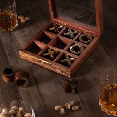 Jogo da velha com peças de metal dourado numa caixa de madeira com tampa de vidro numa mesa rústica