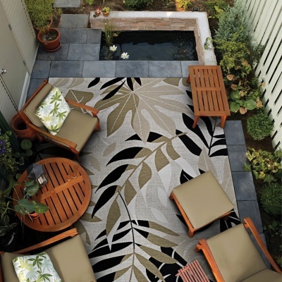 Espaço exterior com mobiliário de madeira, almofadas e tapete com padrão de folhas
