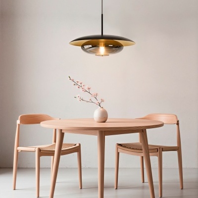 Mesa de madeira redonda com duas cadeiras e vaso com flor, sob luminária pendente preta e dourada, parede branca