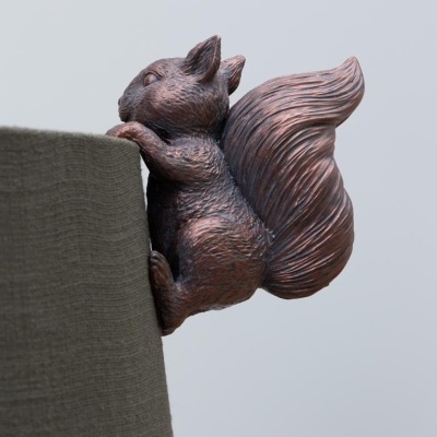 Figura decorativa de esquilo castanho agarrada à superfície cinzenta