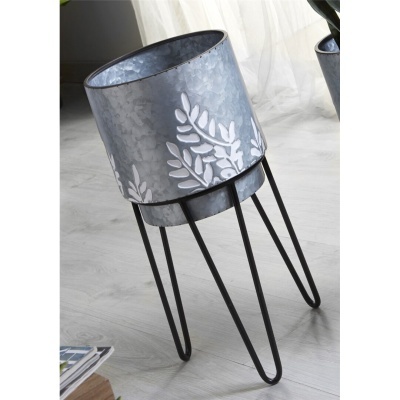 vaso metálico cinza com padrão de folhas brancas em suporte preto de três pernas