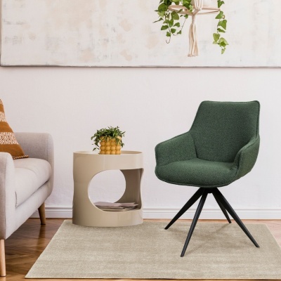 Cadeira verde estofada com base preta, mesa de apoio bege, vaso com planta e sofá cinza num ambiente interior